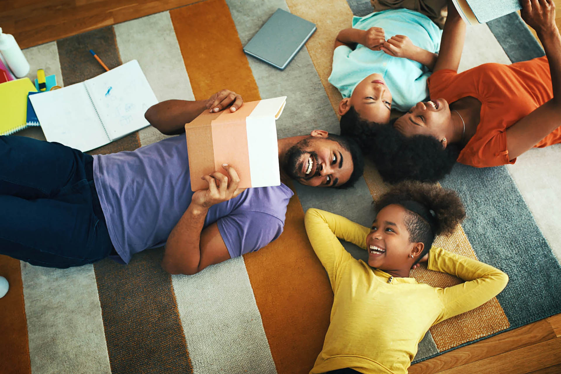 Closeup top view of young african american couple home schooling their children. They are laying on the living room floor and parents are reading to the children during coronavirus quarantine.
